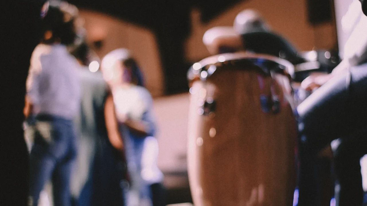 A wooden conga drum in the foreground with dancers blurred behind it