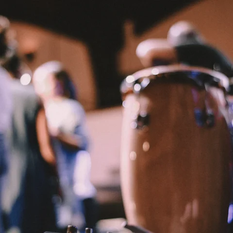 A wooden conga drum in the foreground with dancers blurred behind it