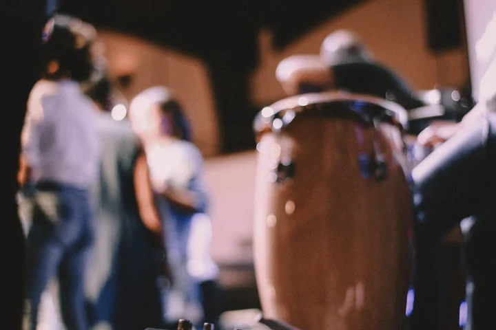 A wooden conga drum in the foreground with dancers blurred behind it