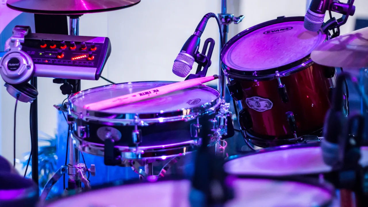 A snare drum and tom fitted with microphones on a stage under purple light, beside a small mixer and headphones
