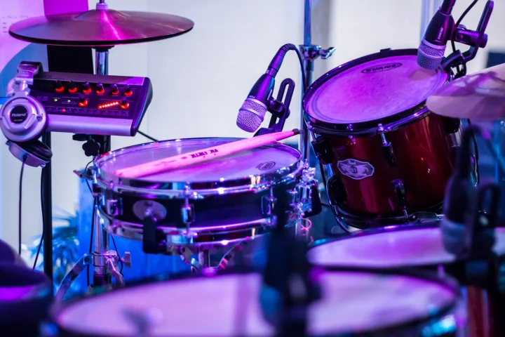A snare drum and tom fitted with microphones on a stage under purple light, beside a small mixer and headphones