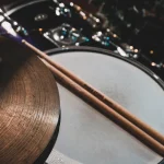 A drumstick resting across a drum next to a cymbal