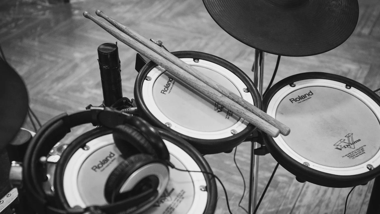 Drumsticks and headphones resting on the mesh pads of an electronic drum kit, in black and white