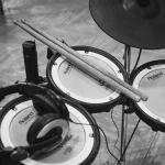 Drumsticks and headphones resting on the mesh pads of an electronic drum kit, in black and white