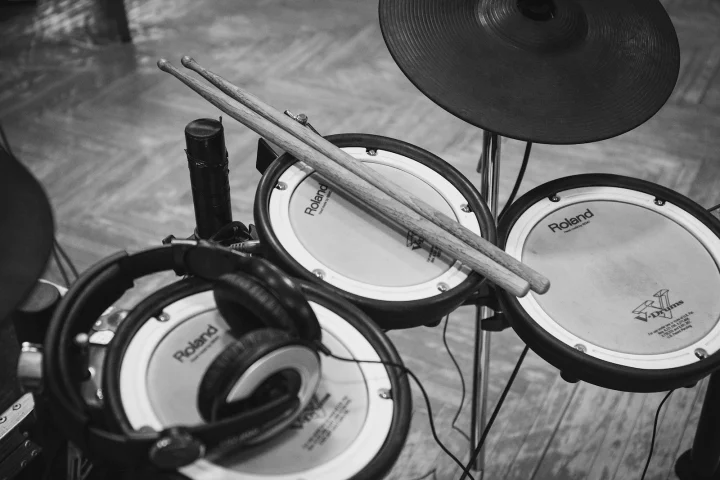Drumsticks and headphones resting on the mesh pads of an electronic drum kit, in black and white