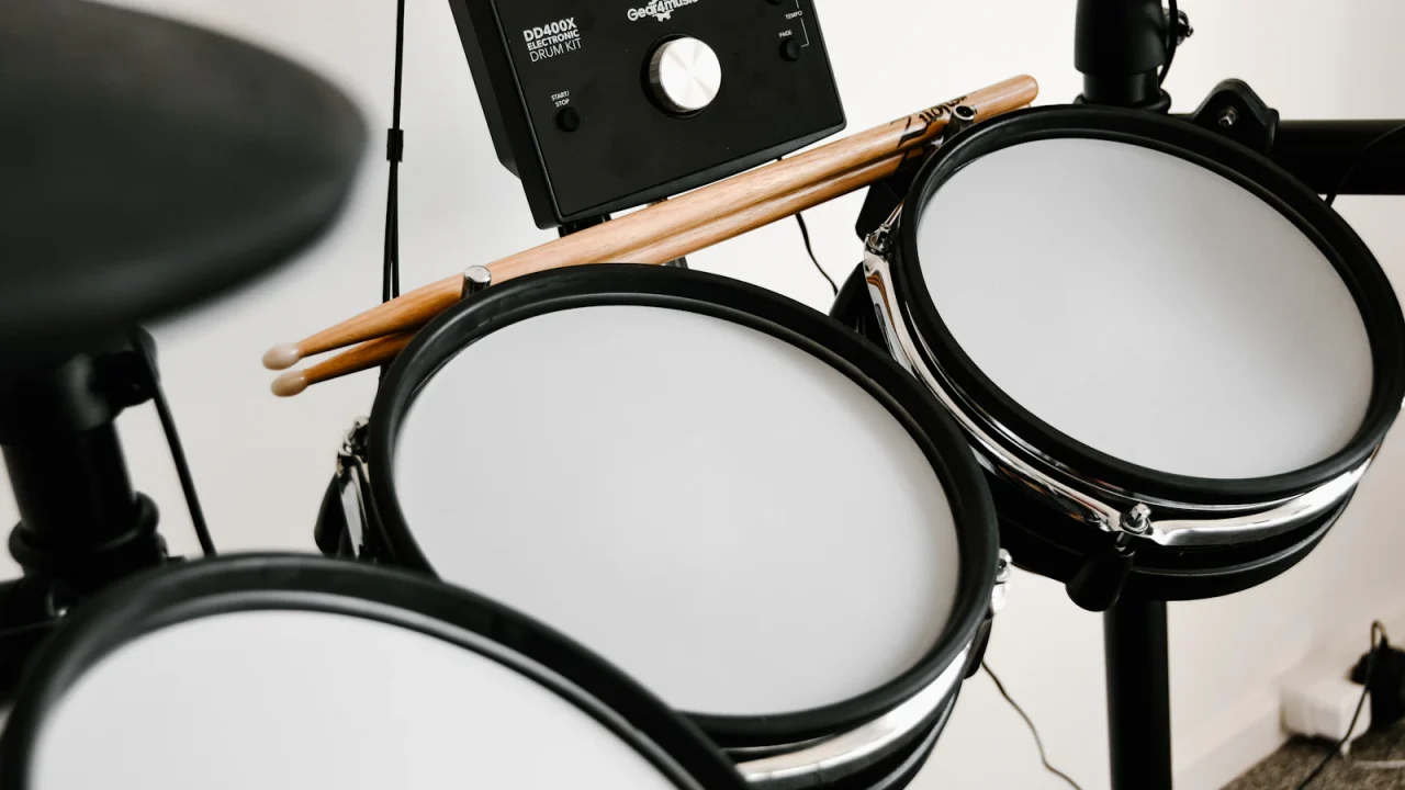 Close-up of drumsticks resting on the mesh pads of an electronic drum kit beside its sound module