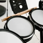 Close-up of drumsticks resting on the mesh pads of an electronic drum kit beside its sound module