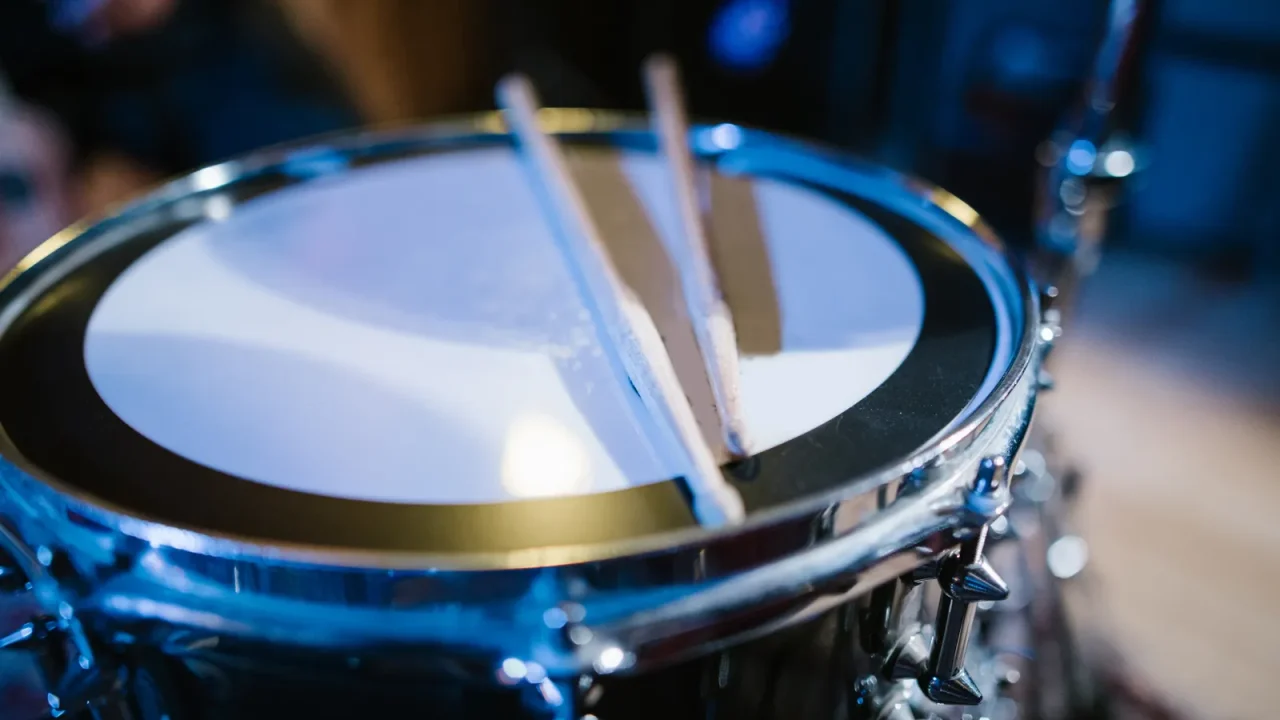 A pair of drumsticks resting on a snare drum under blue light
