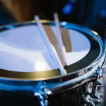 A pair of drumsticks resting on a snare drum under blue light