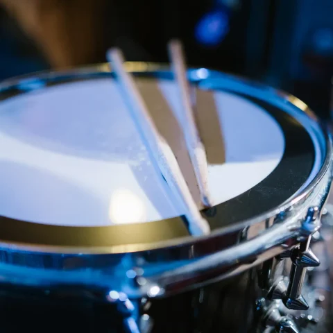 A pair of drumsticks resting on a snare drum under blue light