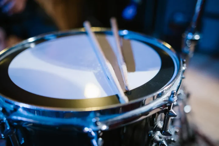 A pair of drumsticks resting on a snare drum under blue light