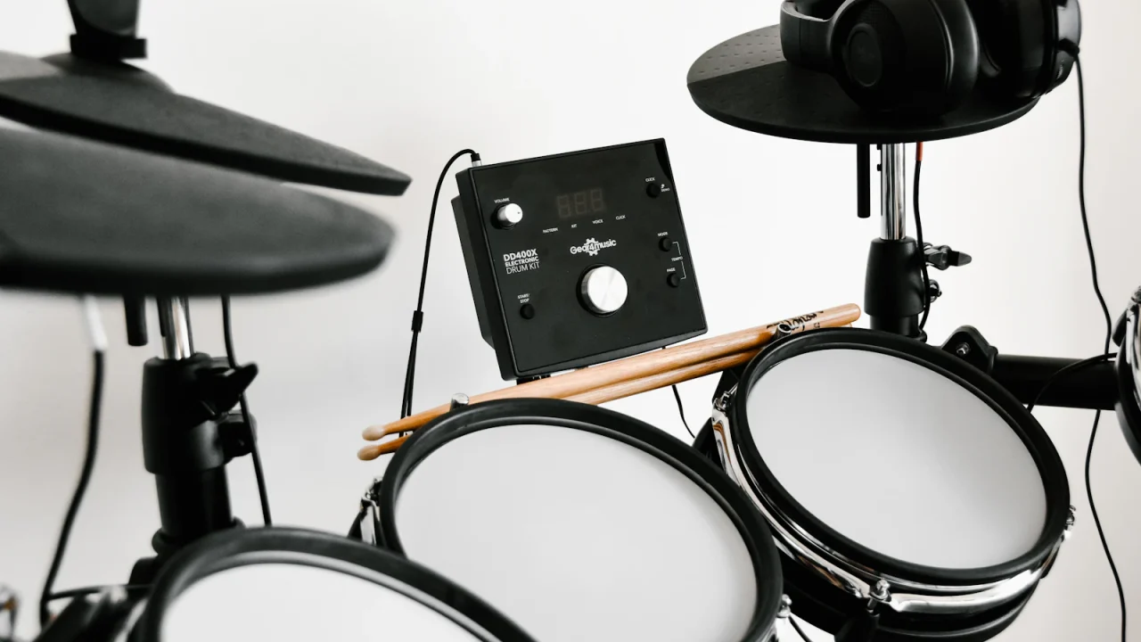 An electronic drum kit with headphones hanging on a cymbal pad and drumsticks resting on the pads