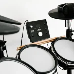 An electronic drum kit with headphones hanging on a cymbal pad and drumsticks resting on the pads