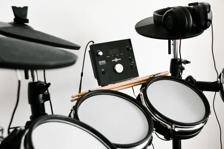 An electronic drum kit with headphones hanging on a cymbal pad and drumsticks resting on the pads