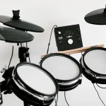 An electronic drum kit with mesh pads, cymbal pads and a sound module against a white wall