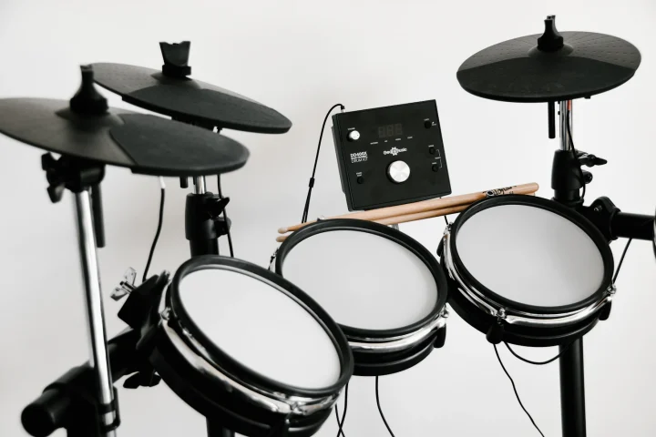 An electronic drum kit with mesh pads, cymbal pads and a sound module against a white wall