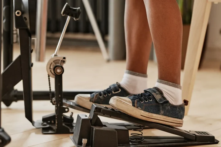 A foot in a sneaker pressing a bass drum pedal