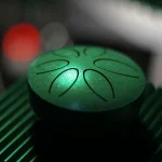 A green steel tongue drum with tongues cut into its top, seen from above