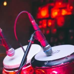 Two hand drums fitted with microphones on a stage under red light