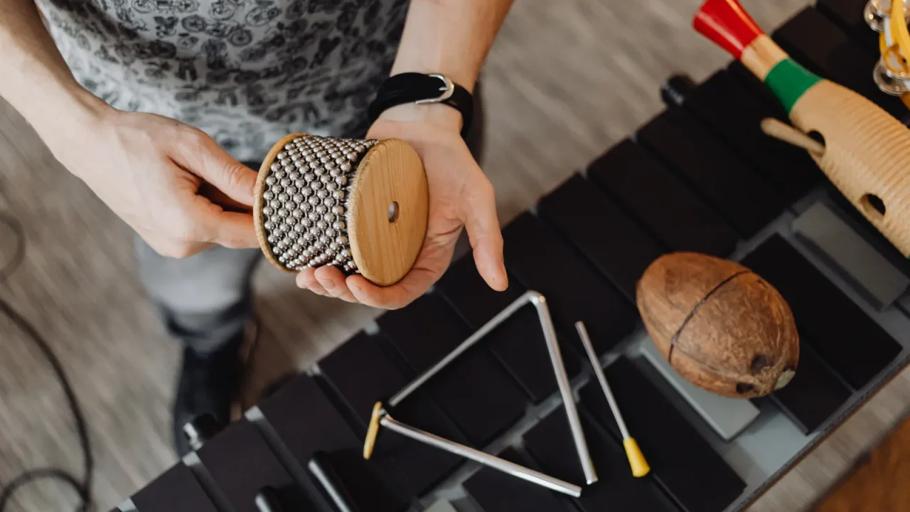 Hands holding a cabasa above a triangle and other small percussion