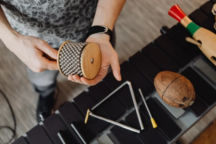 Hands holding a cabasa above a triangle and other small percussion