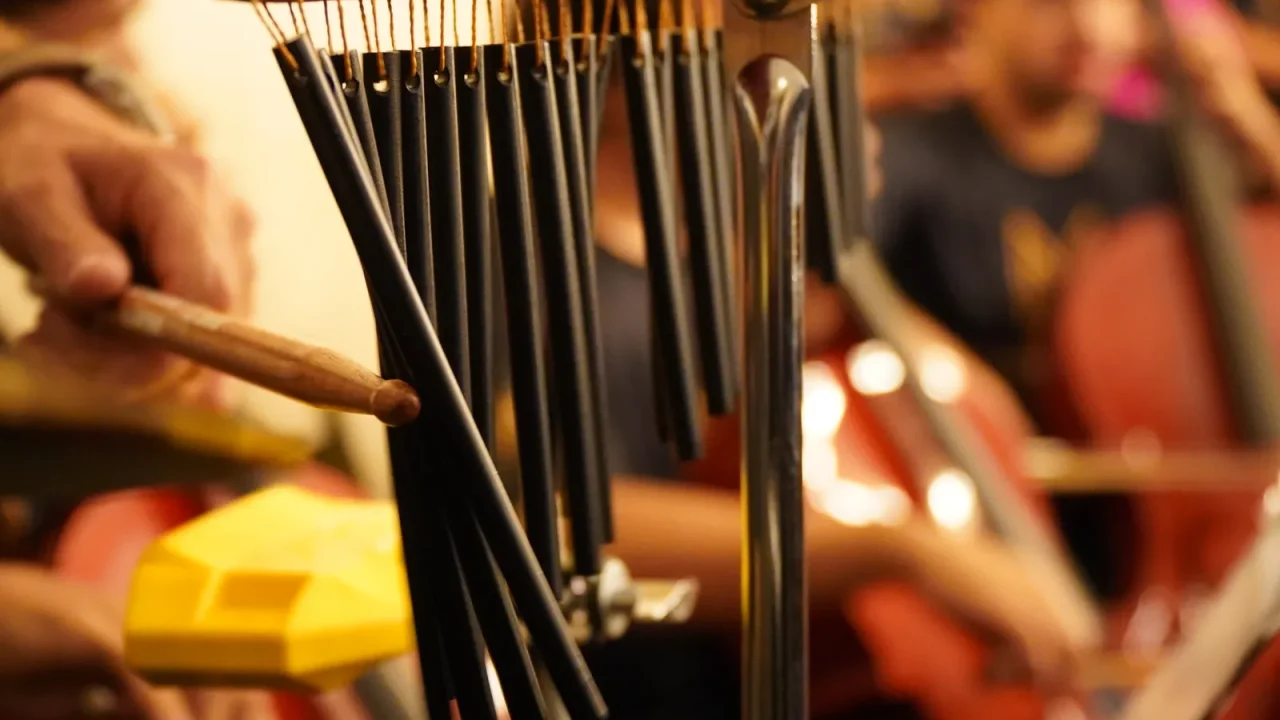 A percussionist striking orchestral chimes during a rehearsal