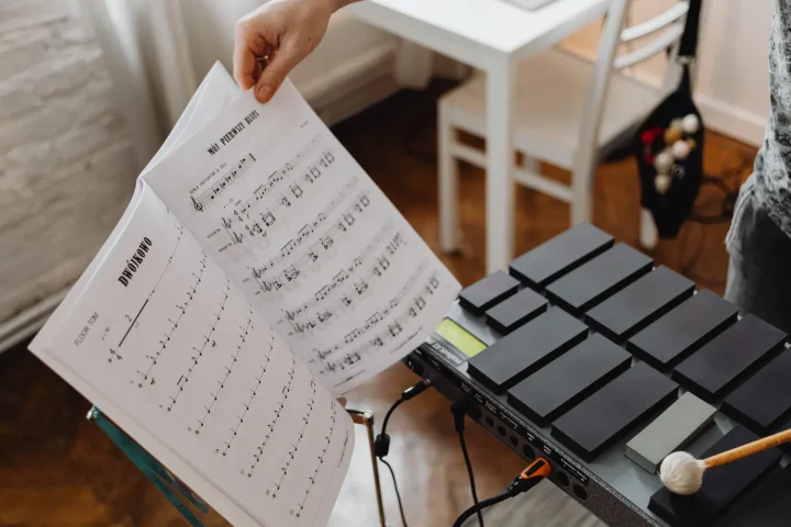 A musician turning pages of sheet music beside an electronic percussion pad